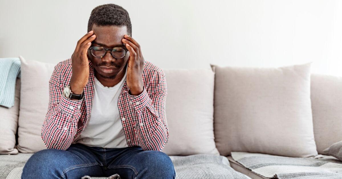 Man holding her head looking downwards with pained expression