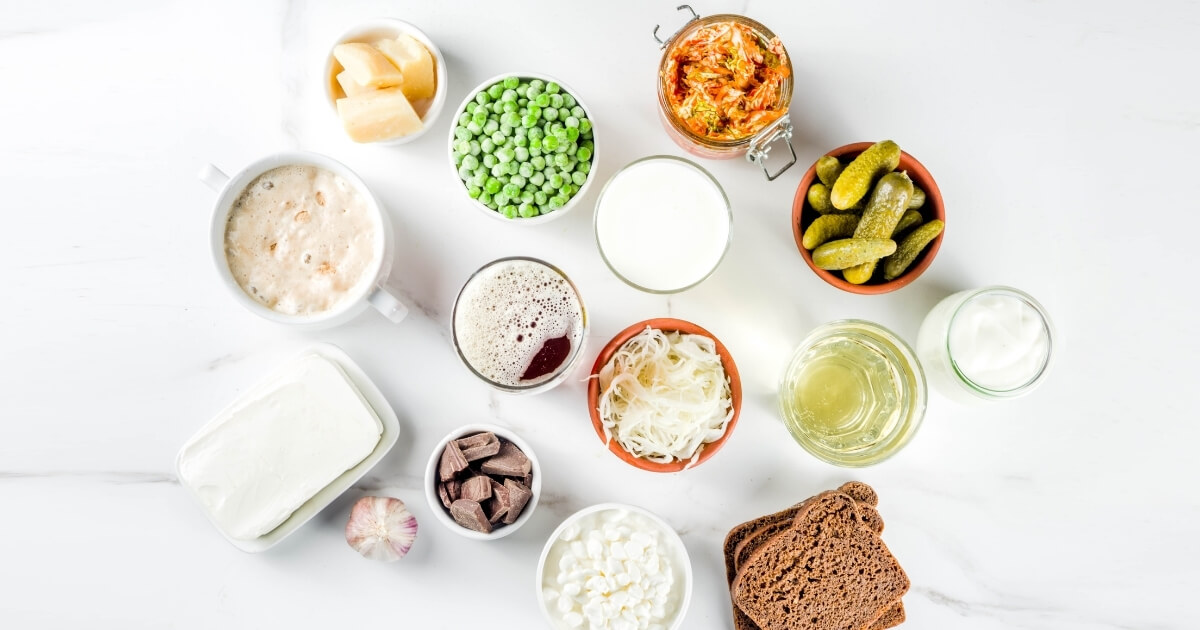 Various foods that support gut health including yogurt, kimchi, lemon water, nuts, greens
