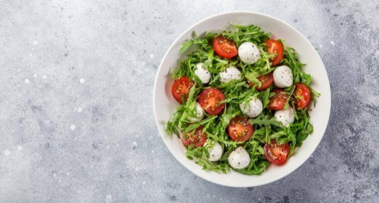 Bowl of salad topped with arugula leaves